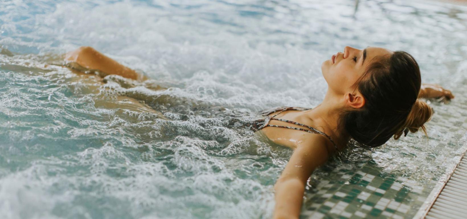 Donna rilassata in piscina con idromassaggio, occhi chiusi, godendo il momento.