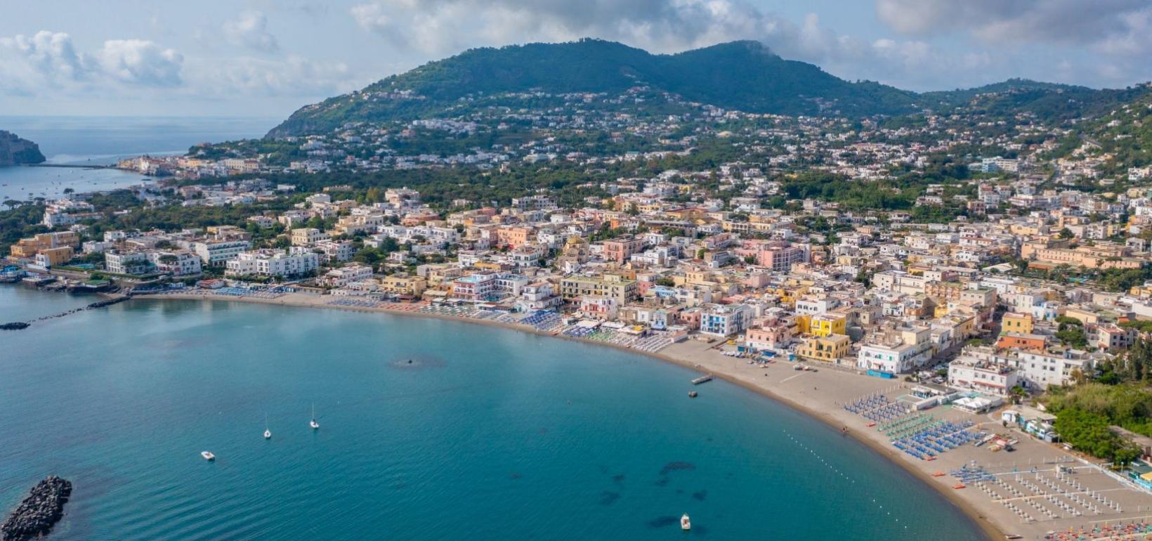 Vista aerea di una città costiera con spiagge, mare blu e colline verdi.